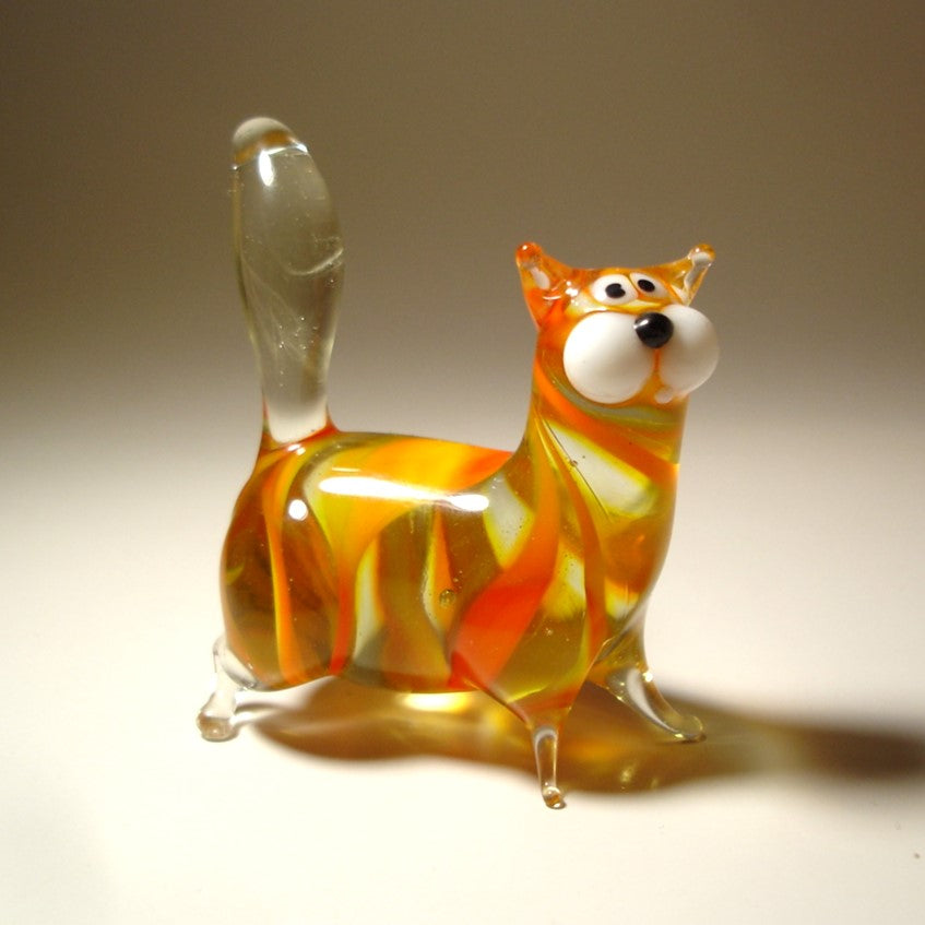 A handmade orange glass chubby cat figurine, standing with its clear glass tail pointed straight up. 