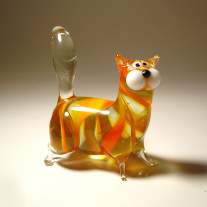 A handmade orange glass chubby cat figurine, standing with its clear glass tail pointed straight up. 