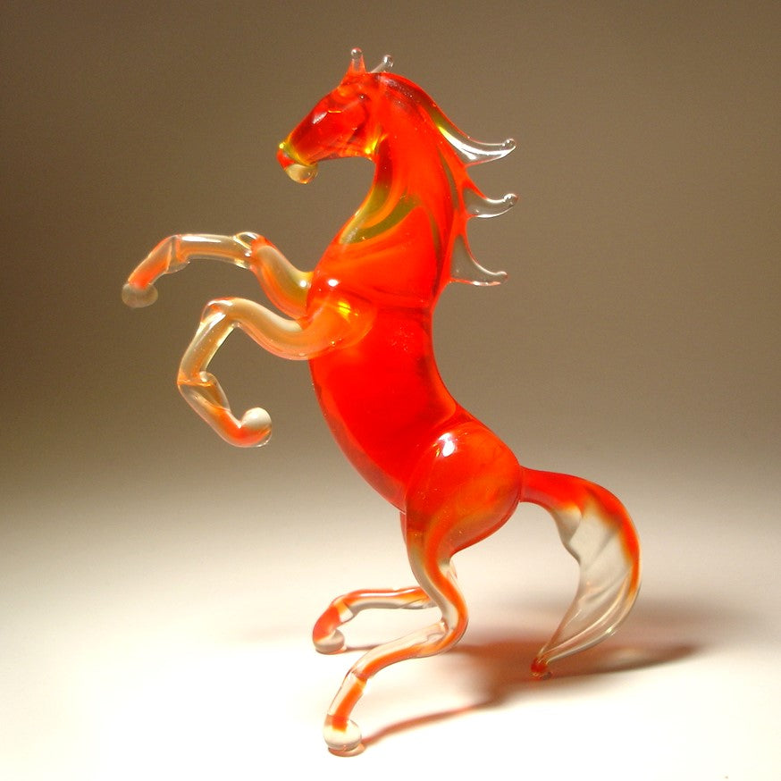 A side view of the red glass horse figurine, highlighting the elegant curves of its rearing body and the flowing tail. 