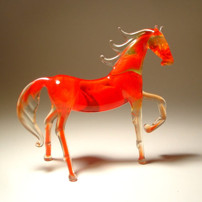A side view of a red glass horse figurine, highlighting its raised left foot and flowing tail.