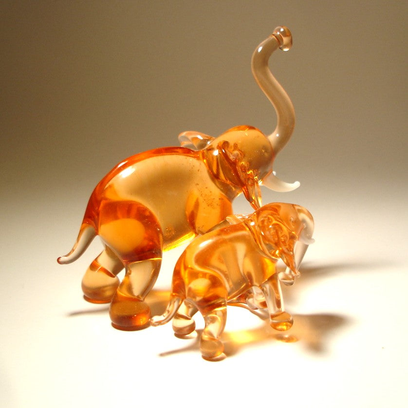 A handcrafted glass elephant figurine with a baby elephant beside it in beige color.