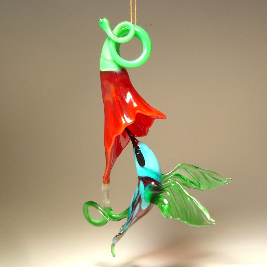 Glass hanging green and blue hummingbird ornament on a red trumpet flower.
