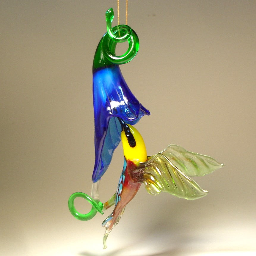 Glass ornament featuring a hummingbird drinking nectar from a blue trumpet flower.