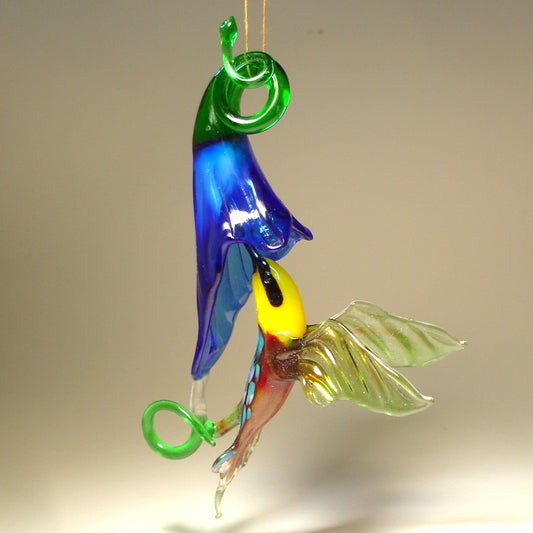 Glass ornament featuring a hummingbird drinking nectar from a blue trumpet flower.