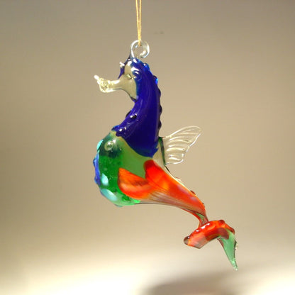A colorful glass seahorse ornament in hues of green, white, and red, gracefully suspended from a thread.