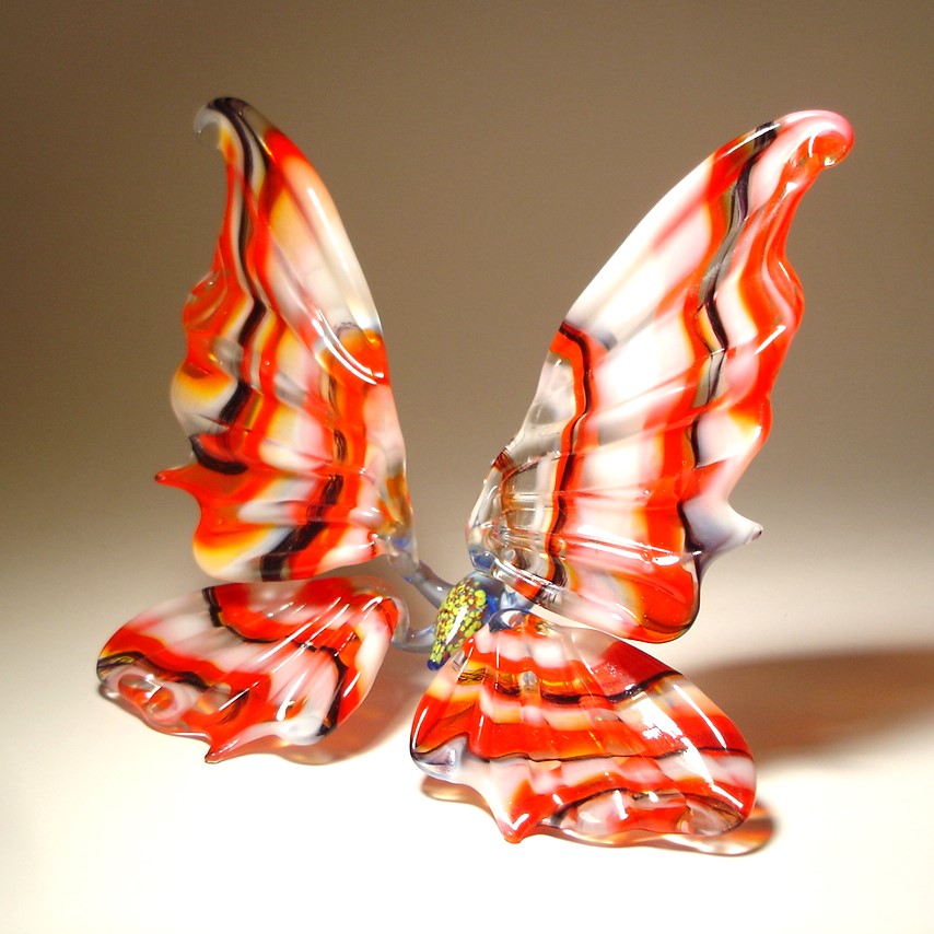 A side view of a red and white striped glass butterfly figurine, highlighting the graceful shape of its wings striped in red, white and black.
