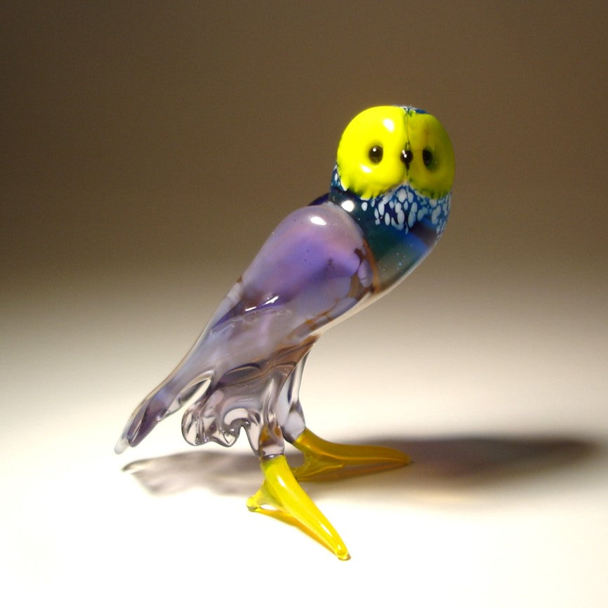 Close-up of a lilac and blue glass owl figurine featuring a bright yellow face and feet.