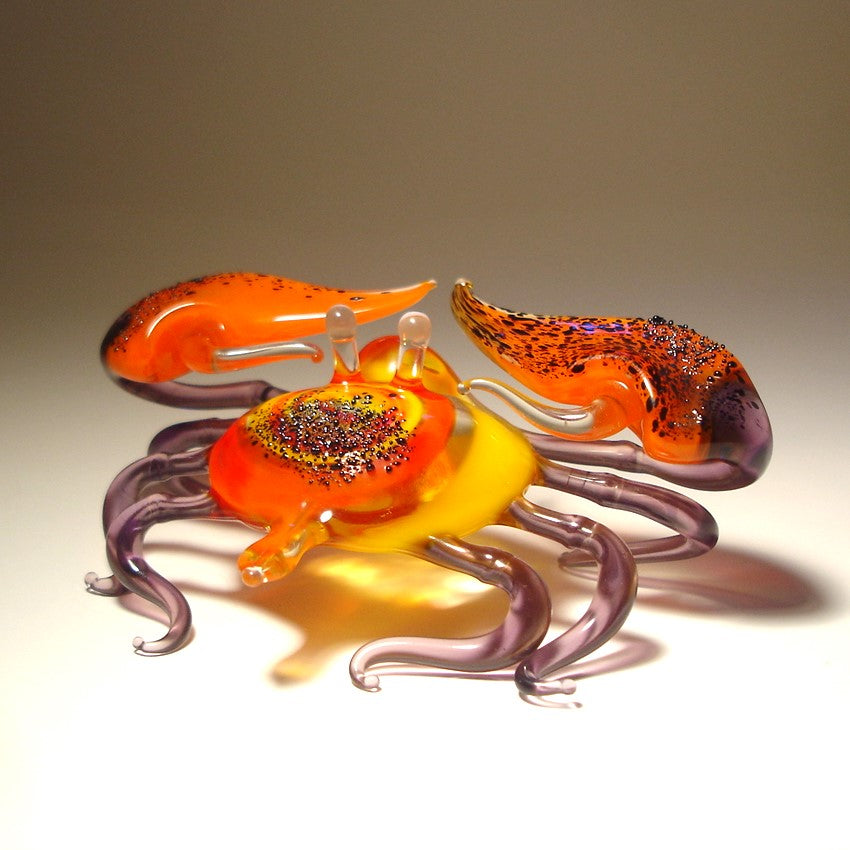 Glass sculpture of a crab with orange, purple, and yellow colors on a beige background.