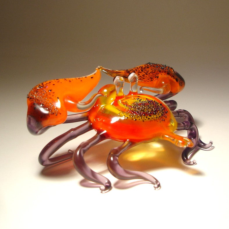 Glass crab sculpture with orange, purple, and yellow colors on a beige background.