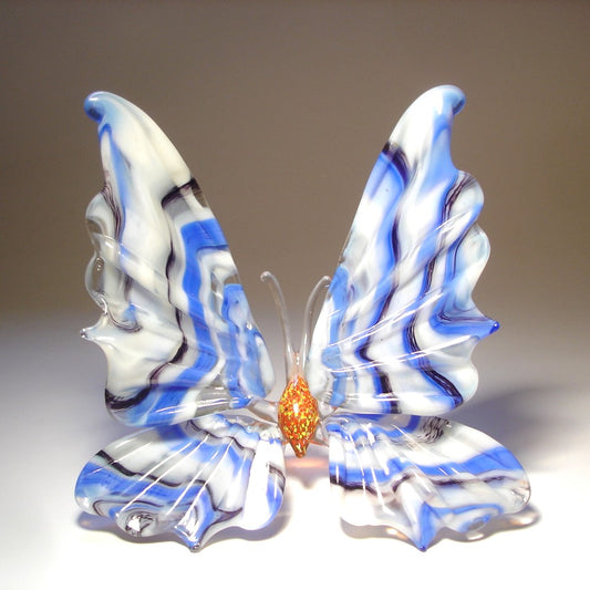 A front view of a white, blue and black striped glass butterfly figurine with intricately designed wings.