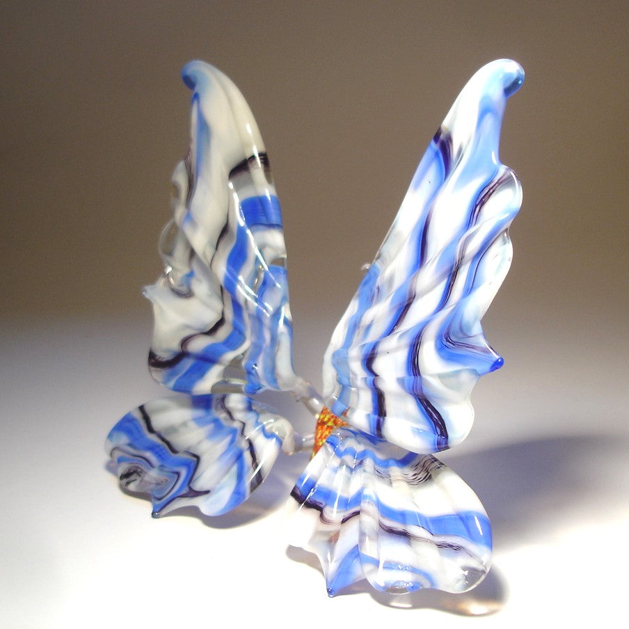 A side view of a white and blue striped glass butterfly figurine, highlighting the elegant curves of its wings and the detailed blue stripes.