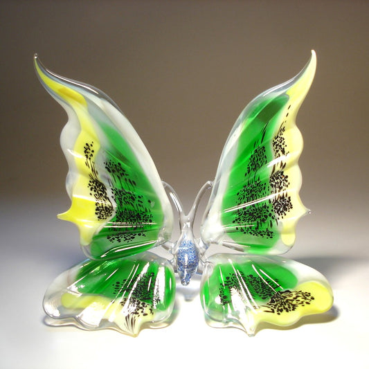 A glass figurine of a butterfly with vibrant green, yellow and black wings, sitting gracefully on a surface. 