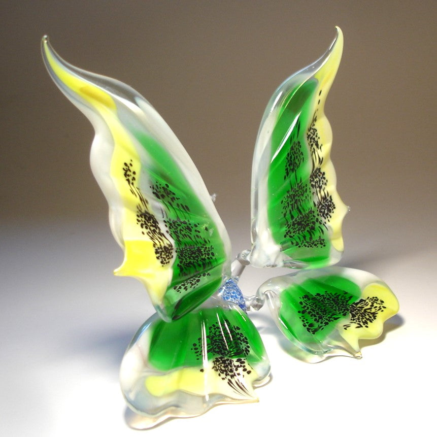 A side view of the glass butterfly figurine, showcasing the slightly raised green and yellow wings and the butterfly's blue body.