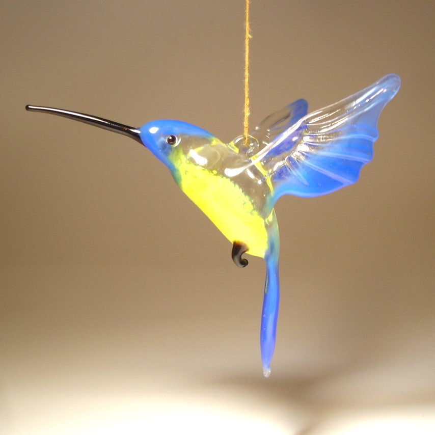 Side view of the blue and yellow glass hummingbird ornament, highlighting elegant shape of its long beak  and blue wings