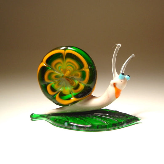 A front view of a glass snail figurine perched on a vibrant green leaf, showcasing its detailed yellow and green shell and delicate face features.