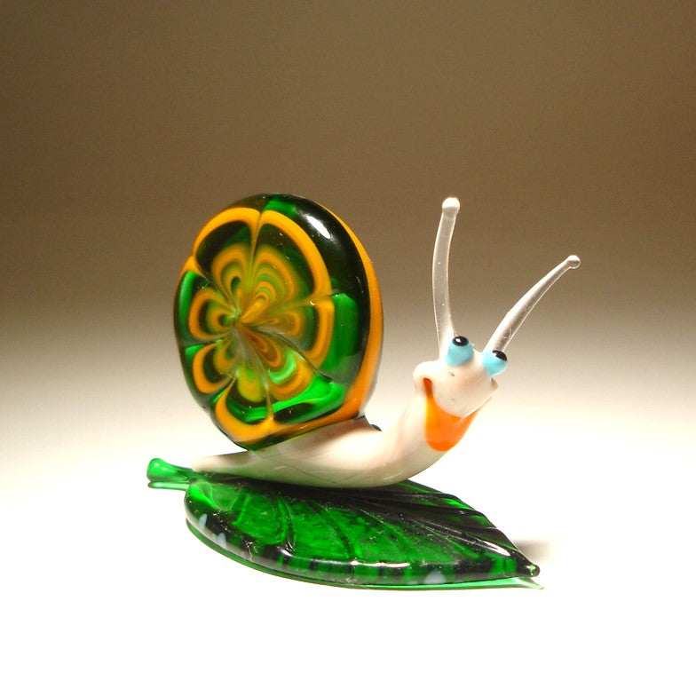 Glass snail figurine with a colorful shell on a leaf against a neutral background