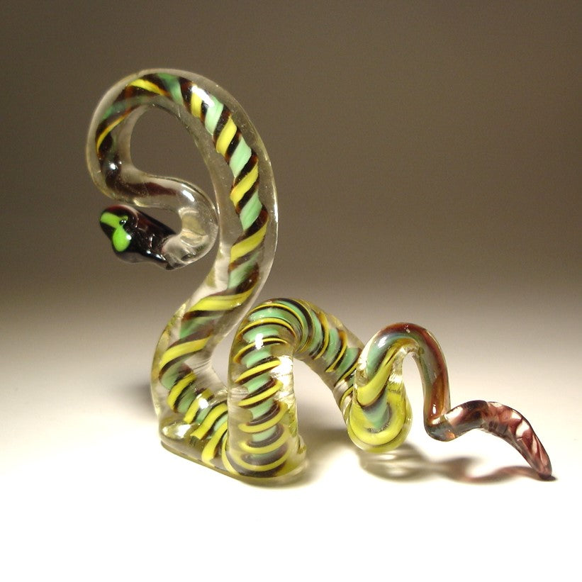 A side view of a glass snake figurine displaying vibrant green, black, and yellow colors, coiled in an agitated pose.