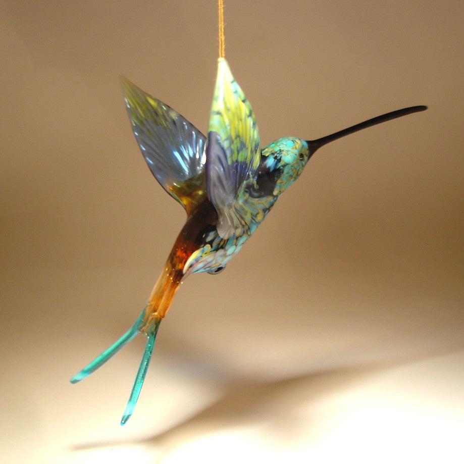 Side view of a glass, blue and Yellow swallowtail hummingbird ornament suspended from a thread.