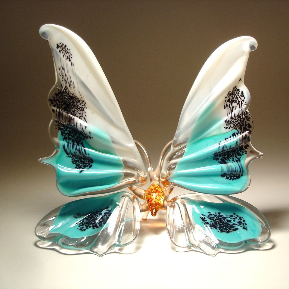 A white and aqua blue  glass butterfly figurine  with red body, sitting.