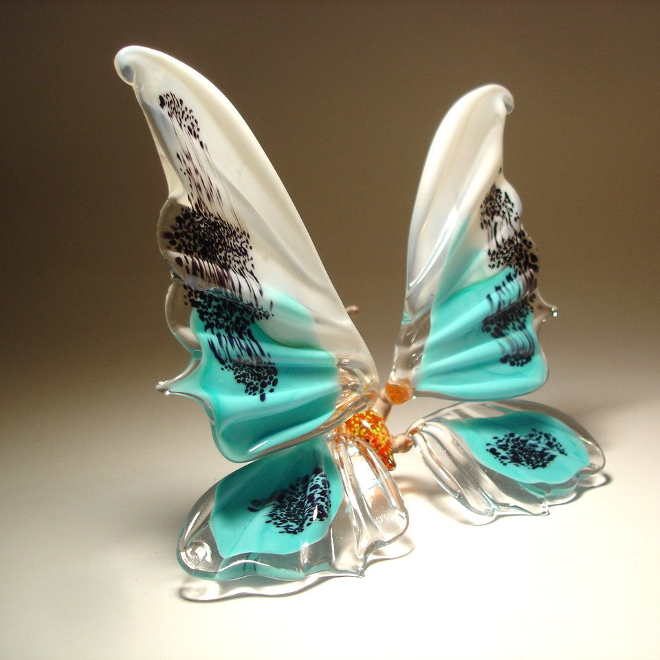 Glass butterfly figurine with turquoise wings and black patterns on a beige background