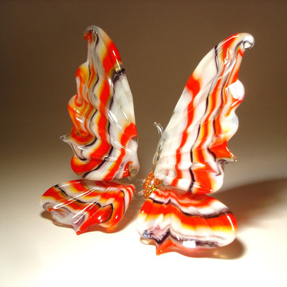 A side view of a red and white striped glass butterfly figurine, highlighting the graceful shape of its wings striped in red, white and black.