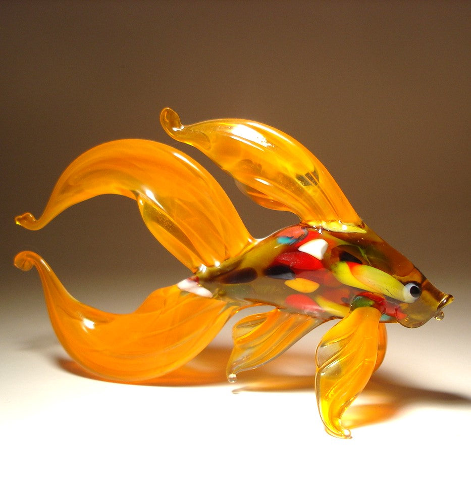 A side view of the orange Betta fish glass figurine, highlighting the flowing, fan-like fins and tail that extend gracefully behind the fish.