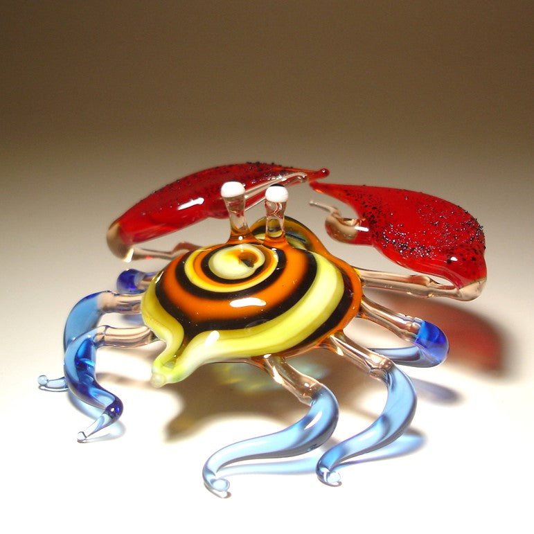 Glass sculpture of a crab with orange, yellow and blue colors on a beige background.