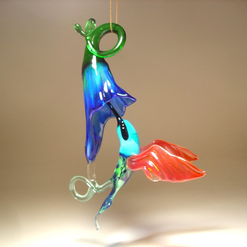Glass red and green hummingbird figurine hovering next to a vibrant blue flower ornament