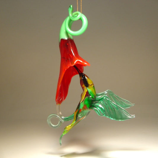 Glass hanging green and yellow hummingbird ornament on a red trumpet flower.