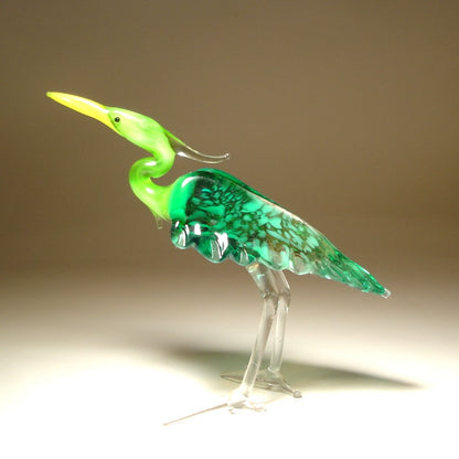 A side view of the glass heron figurine highlighting its green back and intricate feathers on the side of its body.