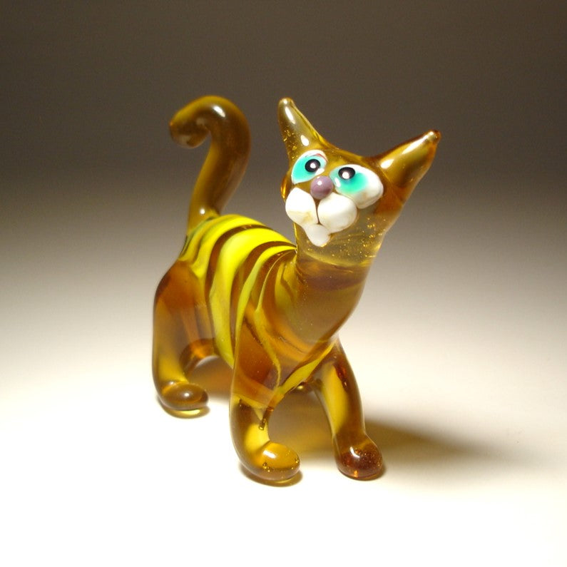 A small glass cat figurine with amber-brown and yellow marbled body, white muzzle and paws, and large turquoise and white eyes.