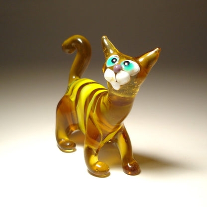A small glass cat figurine with amber-brown and yellow marbled body, white muzzle and paws, and large turquoise and white eyes.