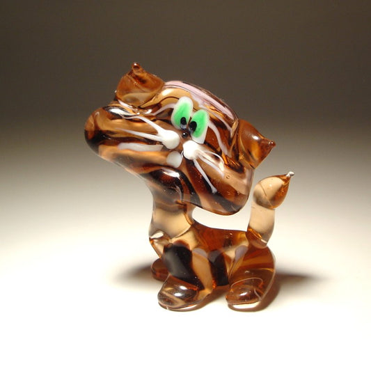 A hand-blown glass cat figurine with a marbled pattern of brown, amber, and white swirls, featuring bright green glass eyes and white whiskers.