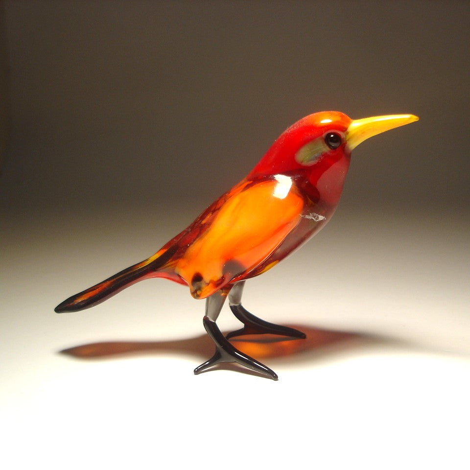 A vibrant glass red bird figurine standing upright, featuring a yellow beak and black tail.