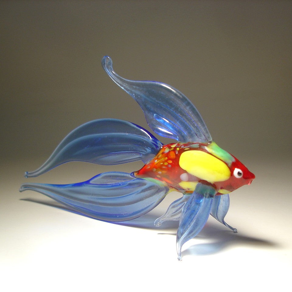 A hand-blown glass fish sculpture with translucent blue fins, a red body, and yellow and green accents.