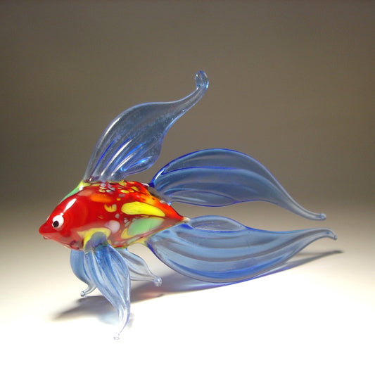 left side view of a hand made blue glass betta fish figurine, showcasing its flowing blue fins and red and yellow body