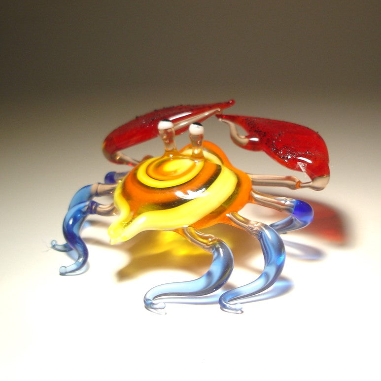 Glass sculpture of a crab with orange, yellow and blue colors on a beige background.