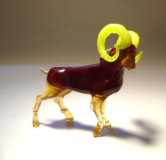 Close-up of a handmade glass mountain goat figurine featuring striking yellow curled horns. 