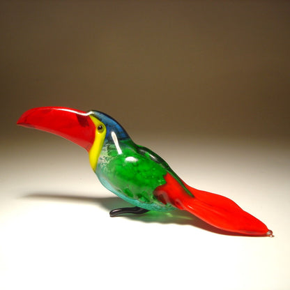 A front view of a glass toucan figurine featuring a vibrant red beak, showcasing its green and red body with a blue head.
