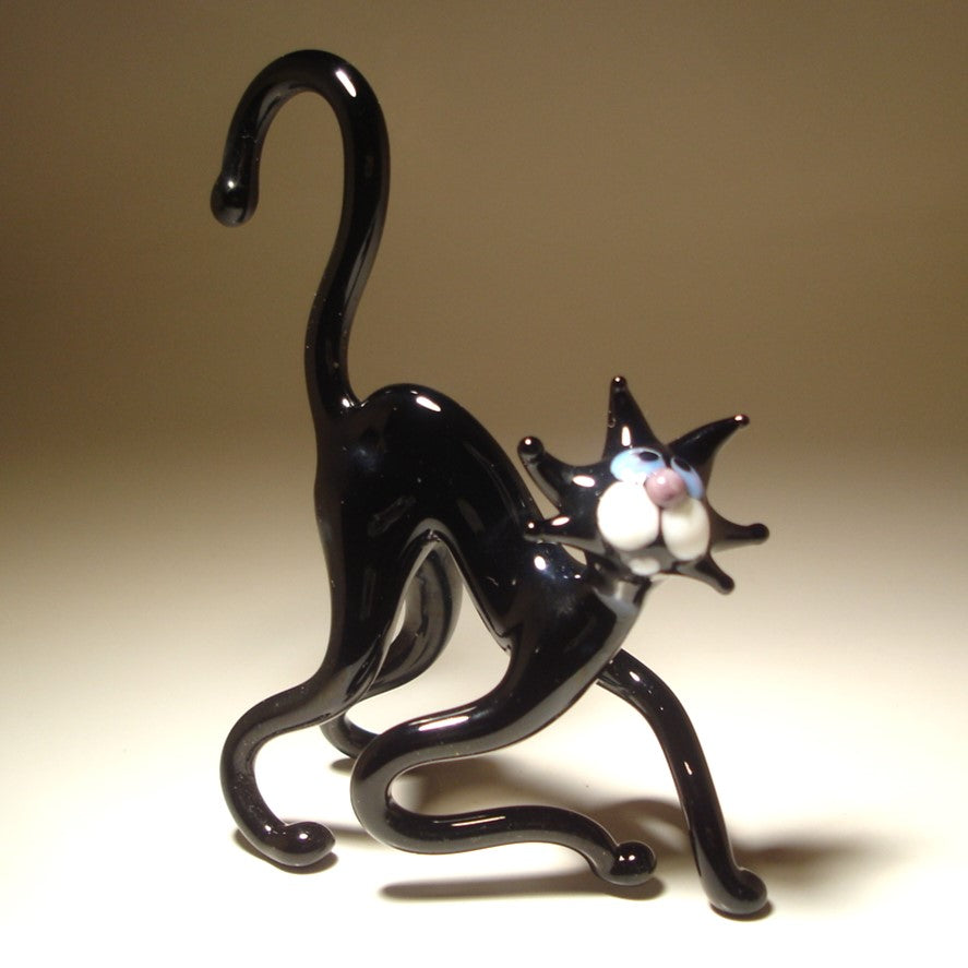 A glossy black glass cat figurine posed in a crouching, playful stance with its tail curved upward.