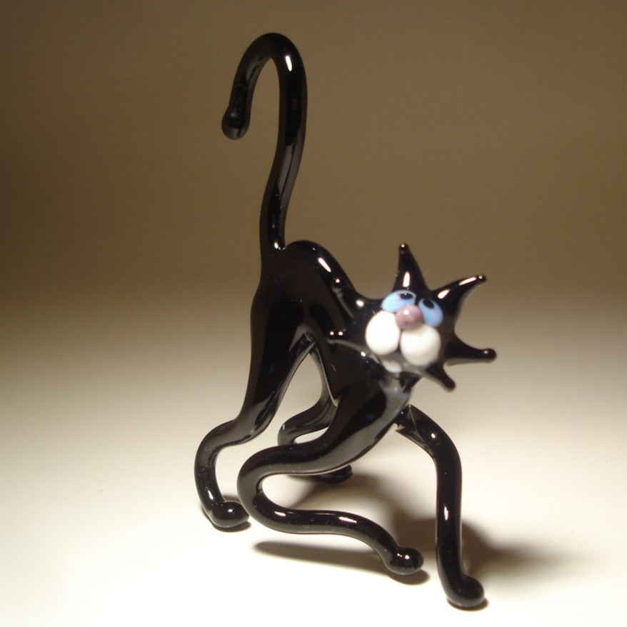 A glass black cat figurine posed in a crouching, stretching stance, with white paws and blue eyes.