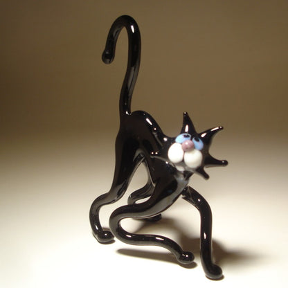 A glass black cat figurine posed in a crouching, stretching stance, with white paws and blue eyes.