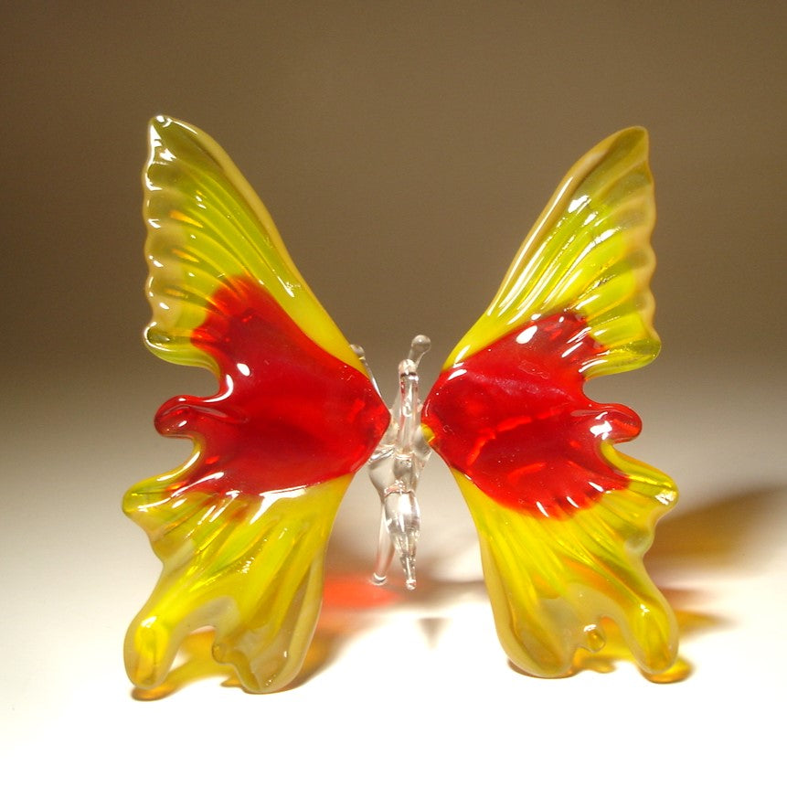 Close-up of a yellow and red glass butterfly ornament, showcasing its yellow and red open wings and intricate detailing. 