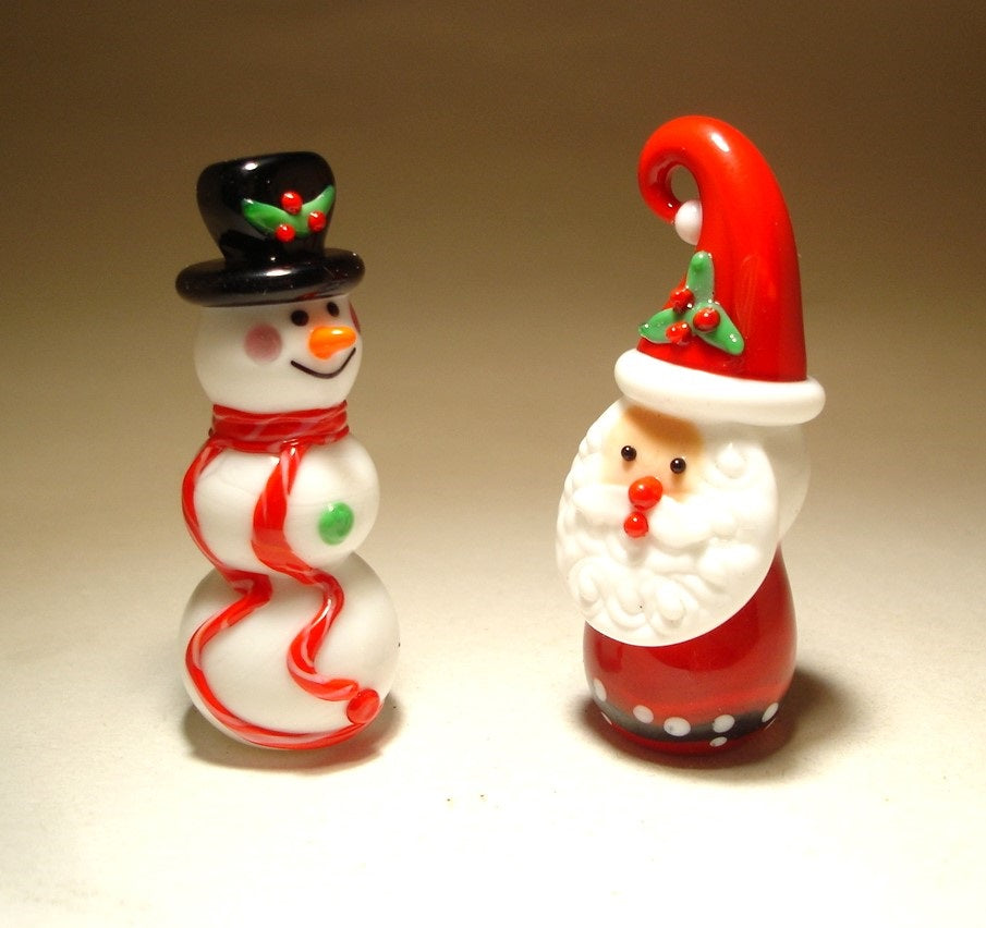 The glass snowman with black bucket hat and red long scarf facing the glass Santa with red hat.