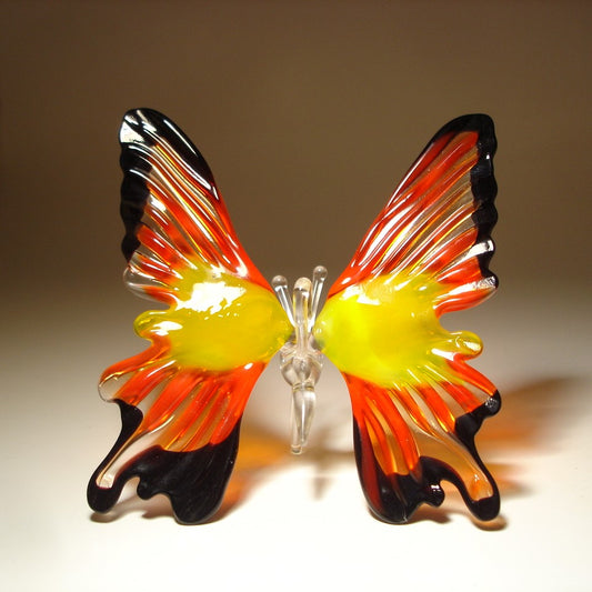 A front view of a red, yellow and black glass butterfly ornament, showcasing its intricate wing patterns and vibrant colors, with clear glass antennae.