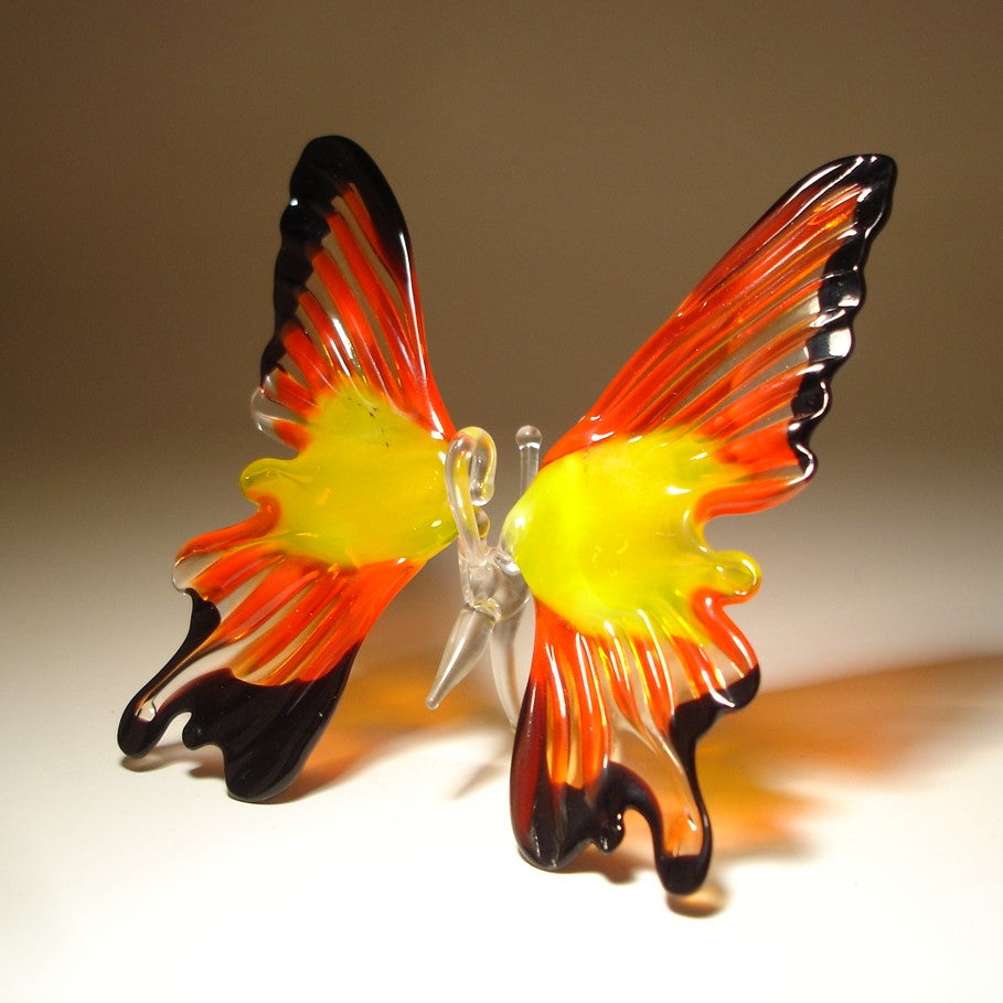 A side view of the red and black glass butterfly ornament, emphasizing the graceful curves of its wings and the contrast between the bold red and deep black.