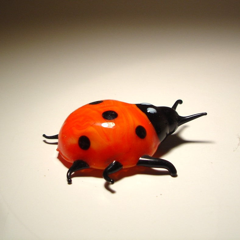 A glossy ladybug figurine with a bright orange-red body, black spots, and a black head and legs.