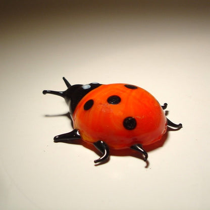 A glossy red ladybug figurine with black spots, black antennae, and black legs