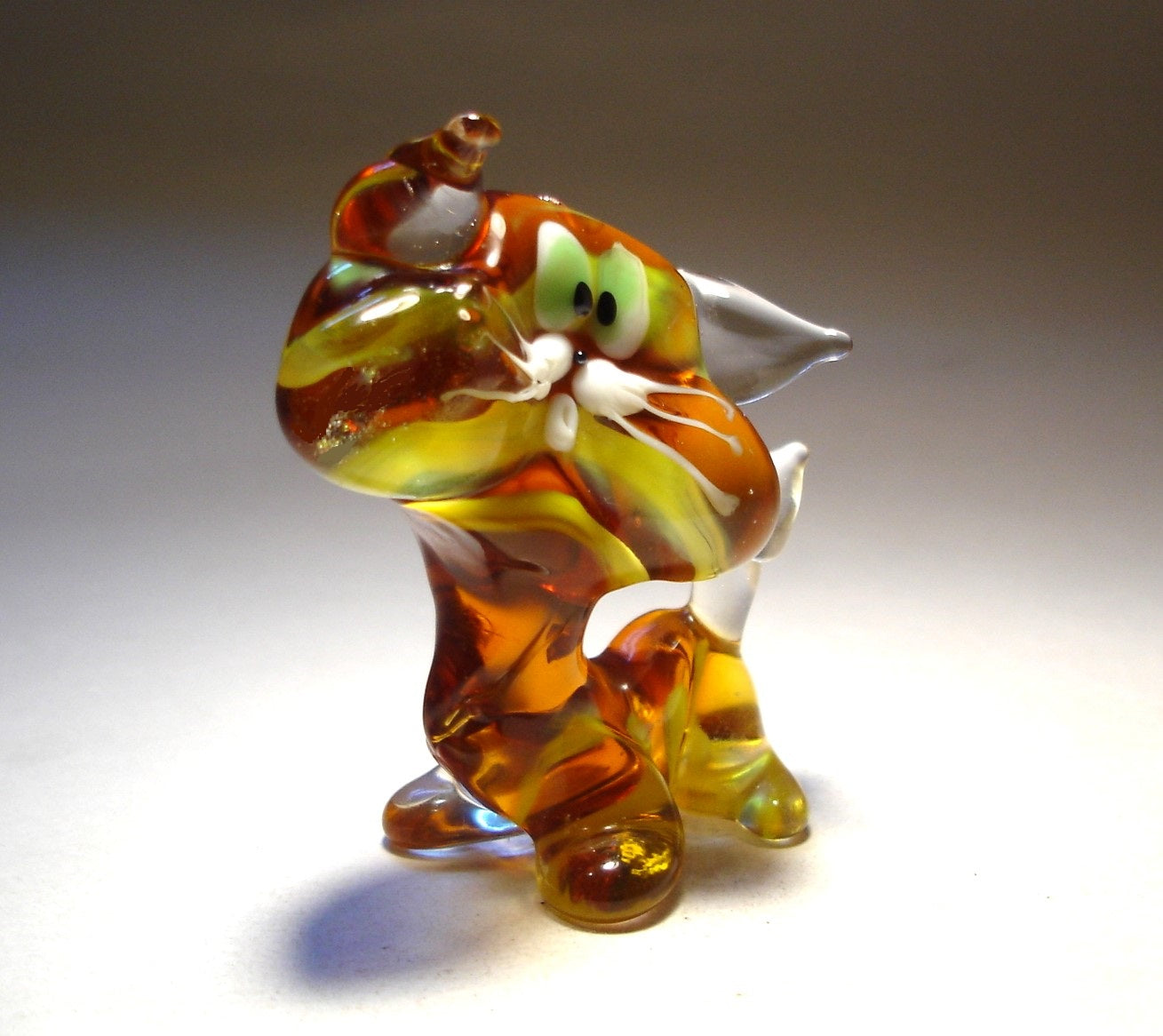 A side view of a glass striped cat figurine, emphasizing its elegant posture and perked clear glass ears.