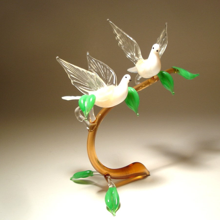 A front view of a glass figurine featuring two white doves perched on a  glass branch, showcasing their outstretched wings in an elegant, peaceful pose.
